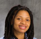 Portrait of Brittany Prempin in a blue shirt on a grey background.