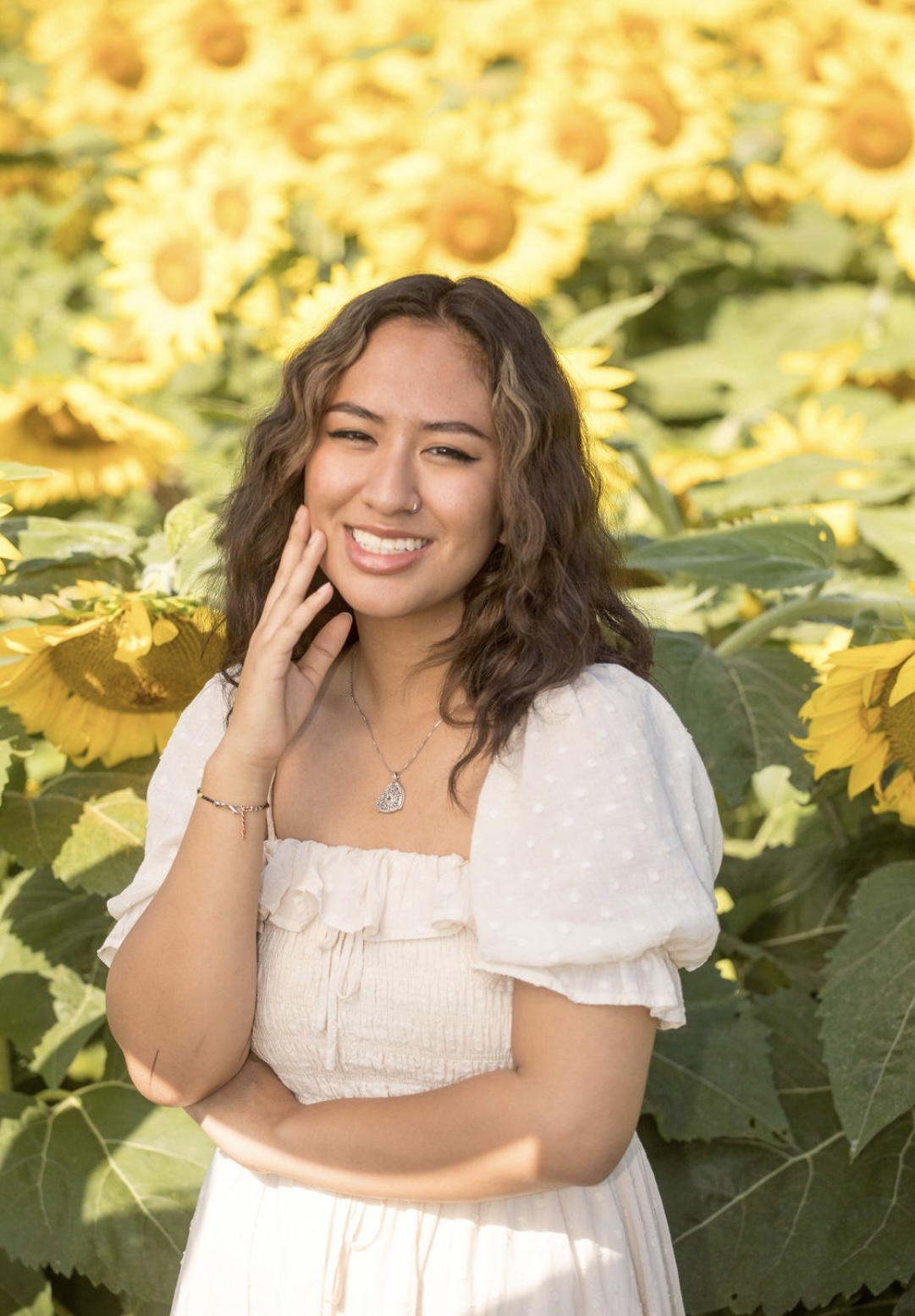 A young woman in a white shirt in front of yellow and green leaves.